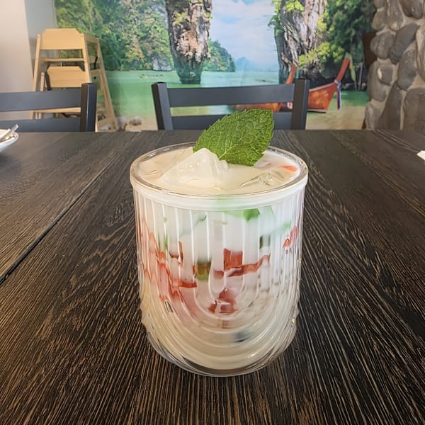 A glass of Thai Iced Tea with ice and mint, on a dark wooden table.