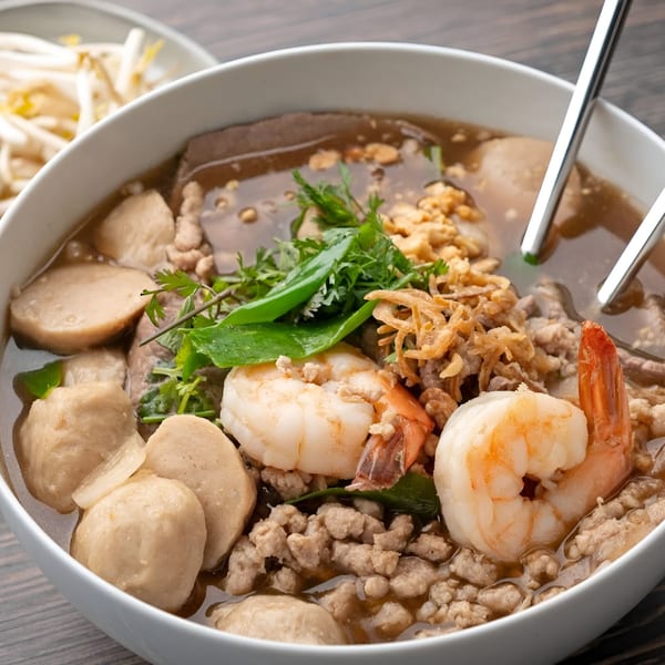 Asian-fusion noodle soup with shrimp, meatballs, minced pork, and herbs, with bean sprouts on the side.
