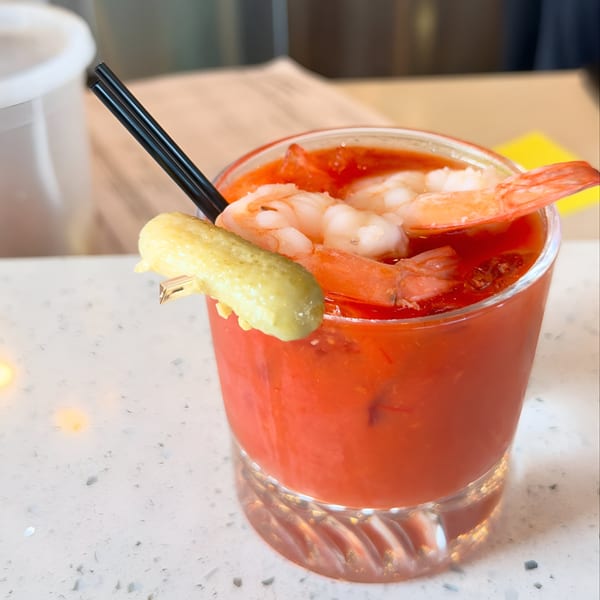 Bloody Mary cocktail garnished with shrimp and a pickle spear, with a black straw.