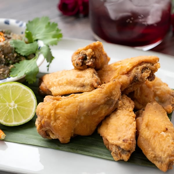 Crispy fried chicken wings with a side of green dipping sauce, lime, and a red drink.