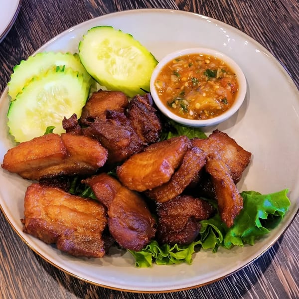 Crispy fried pork belly with fresh cucumber slices and a spicy dipping sauce on a white plate.